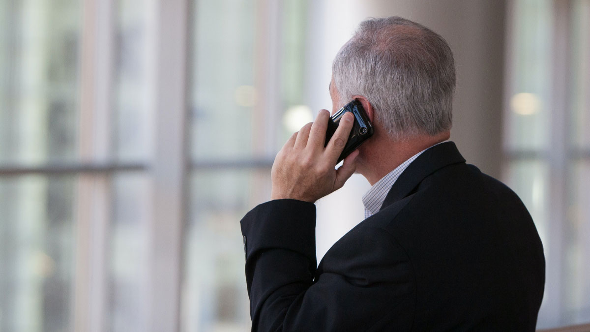 older businessman looking out window while using mobile device
